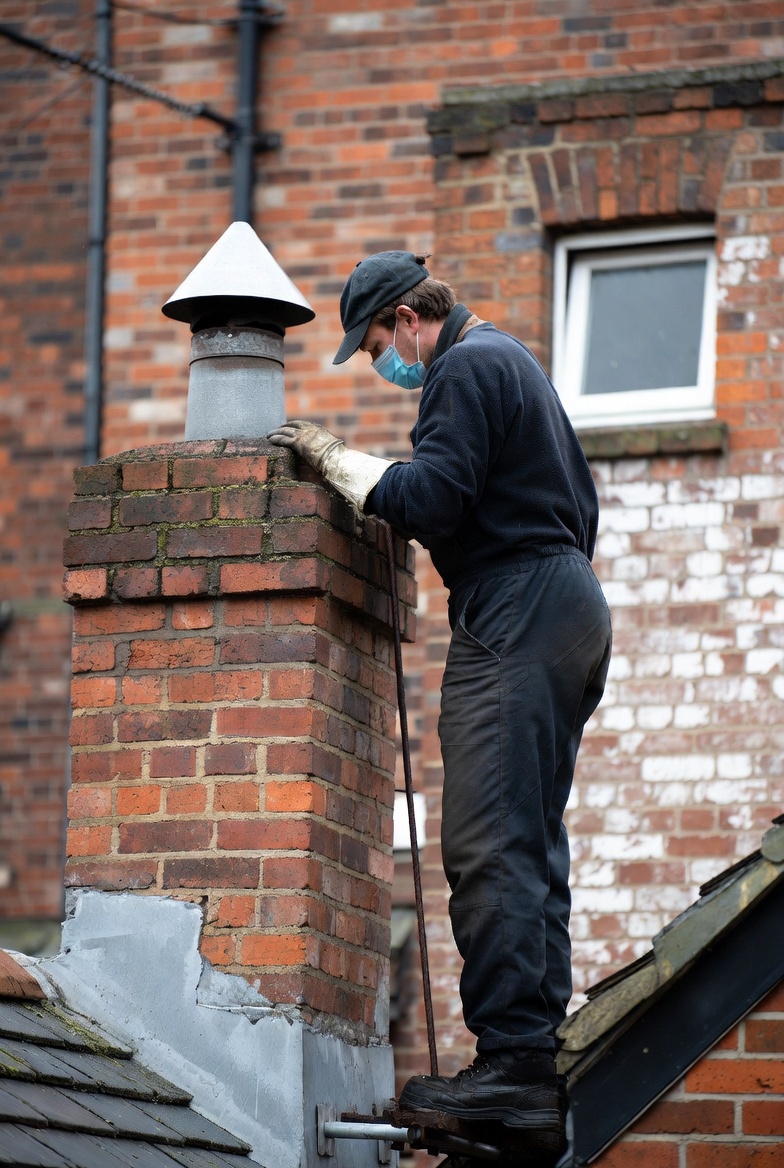 A chimney sweep technician inspecting and cleaning a residential chimney and fireplace system with professional tools