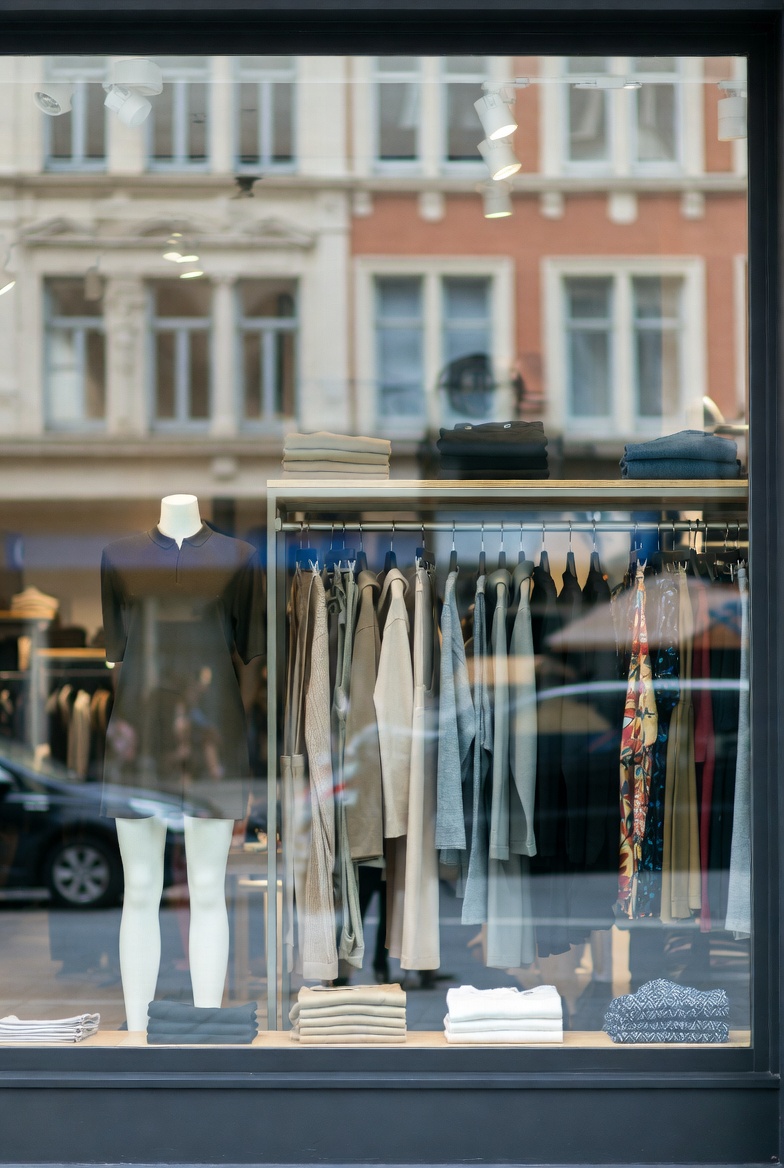 A bright clothing store interior with apparel racks, mannequins, and shoppers browsing seasonal collections