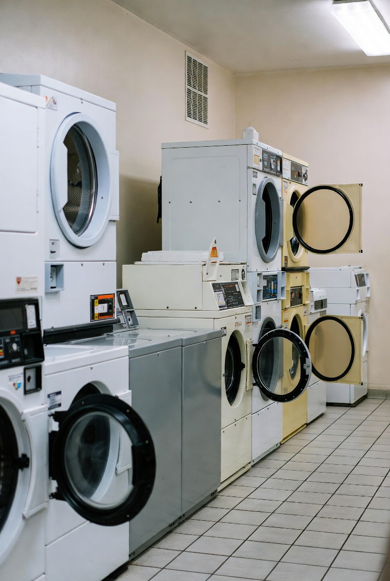 A modern self-service laundromat with rows of commercial washers and dryers, folding tables, and bright clean interiors